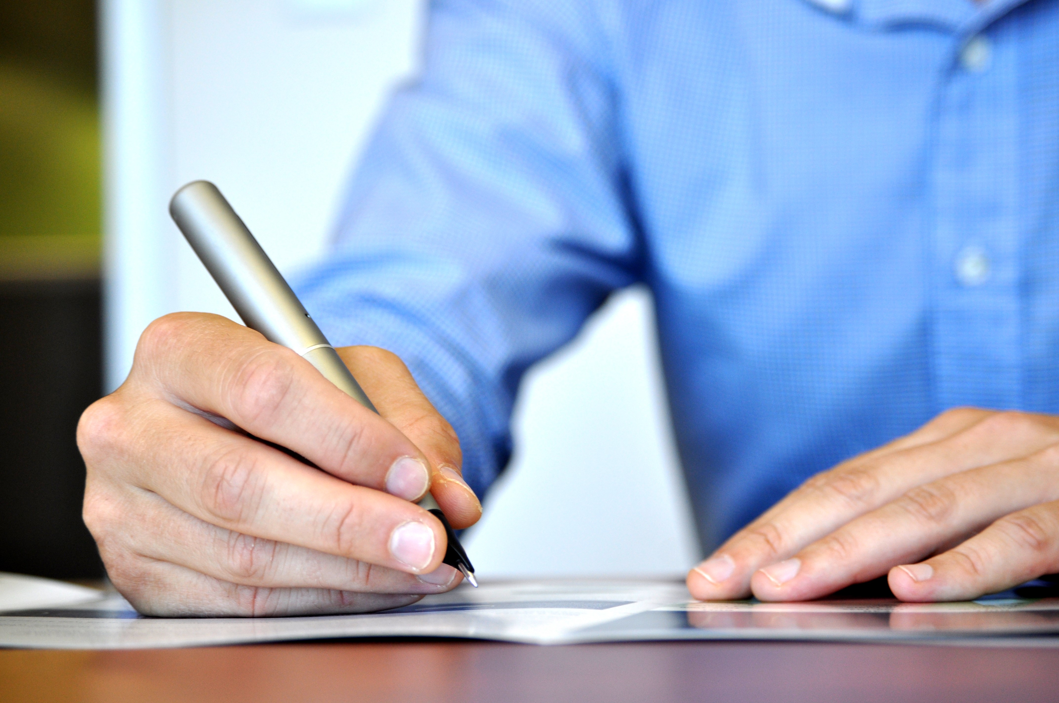  A person in a blue shirt is writing on a piece of paper with a pen. The image represents the search query 'Professional CV review services'.
